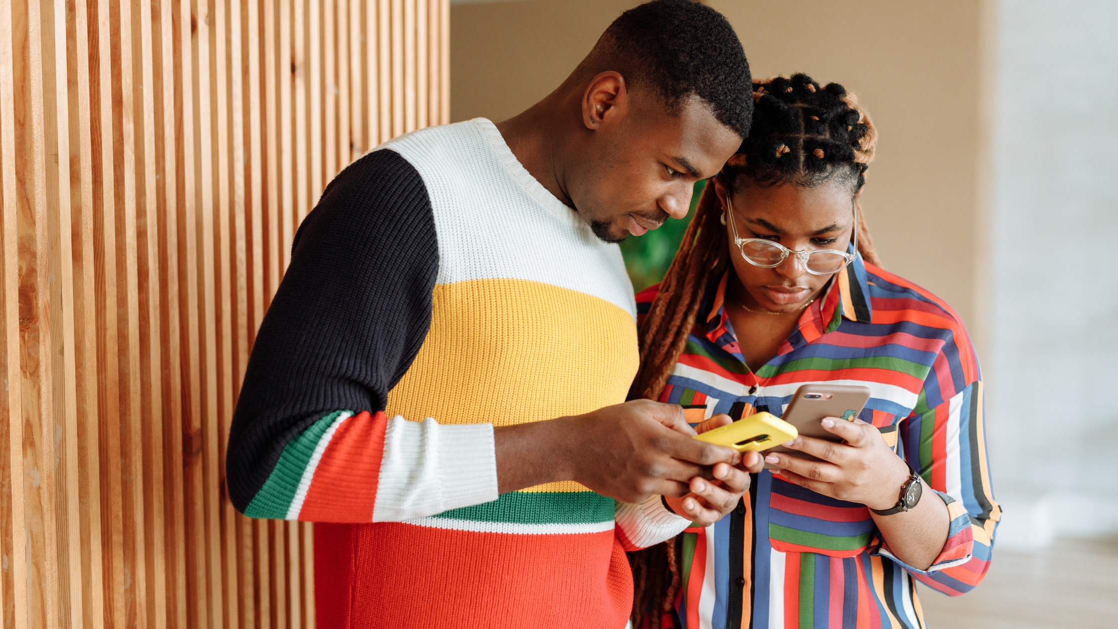 Photo of a man in a knitted sweater and a woman in a colourful shirt using their mobile phones