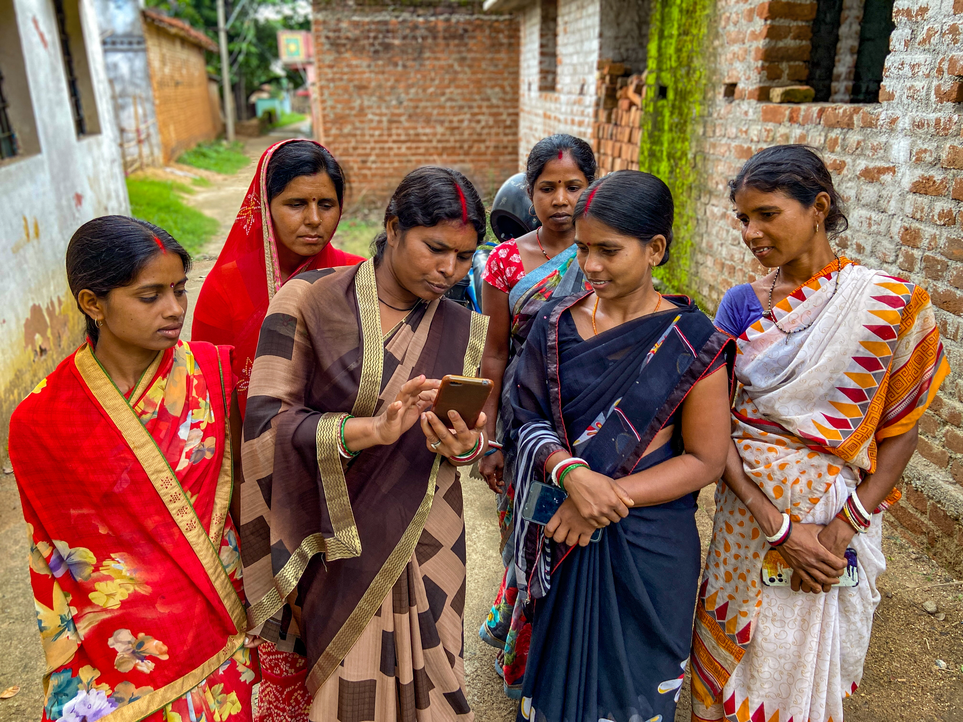 A group of women from rural India looking at the smartphone one of them is holding. 