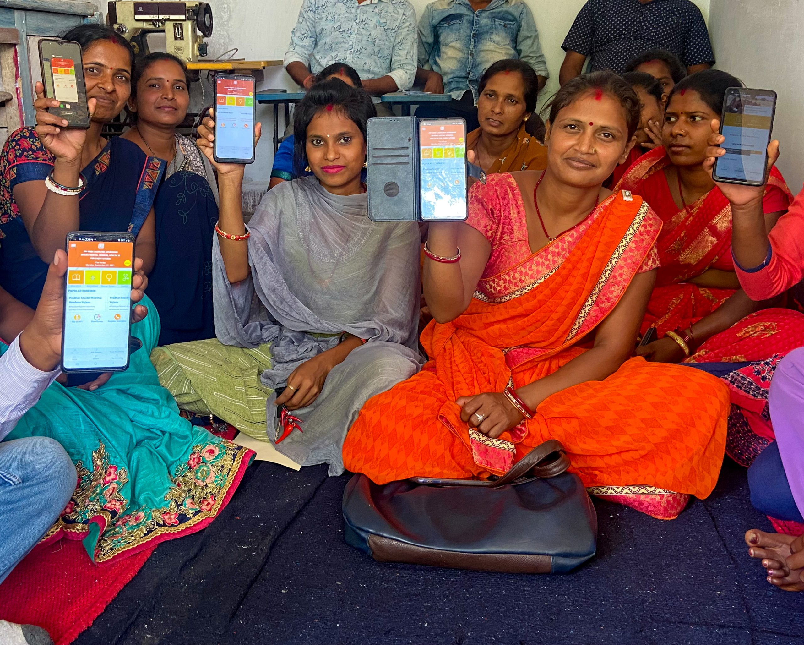 A group of women sitting in a room showing the MeraApp on their smartphones