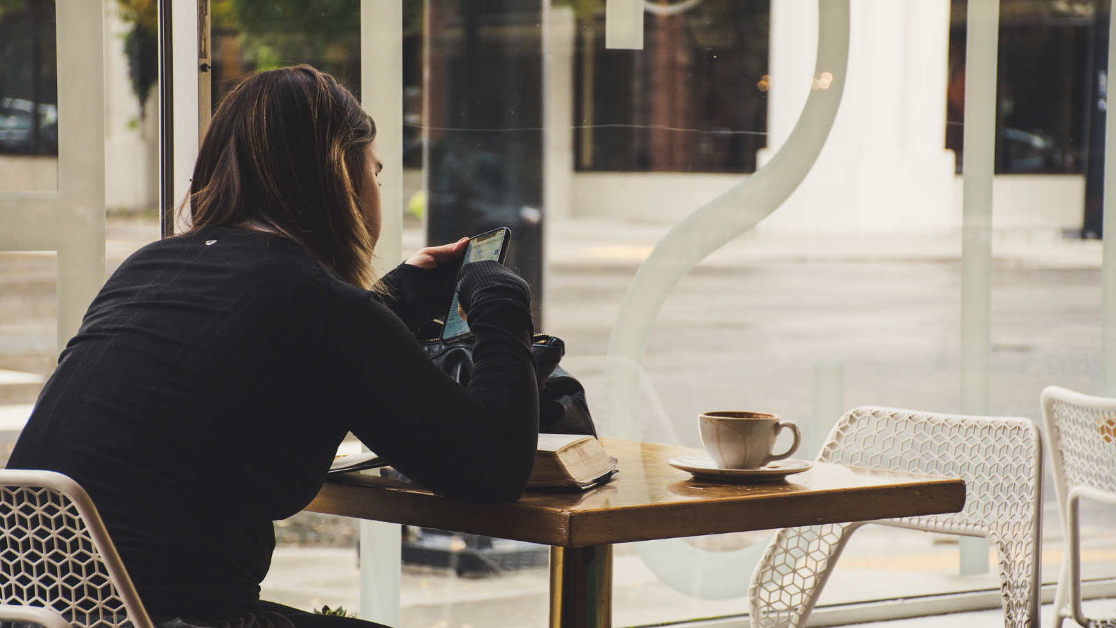 A woman using her smartphone in a coffee shop while reading