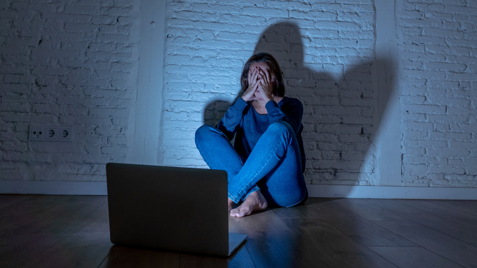 Sad and scared woman covering her face in front of a computer