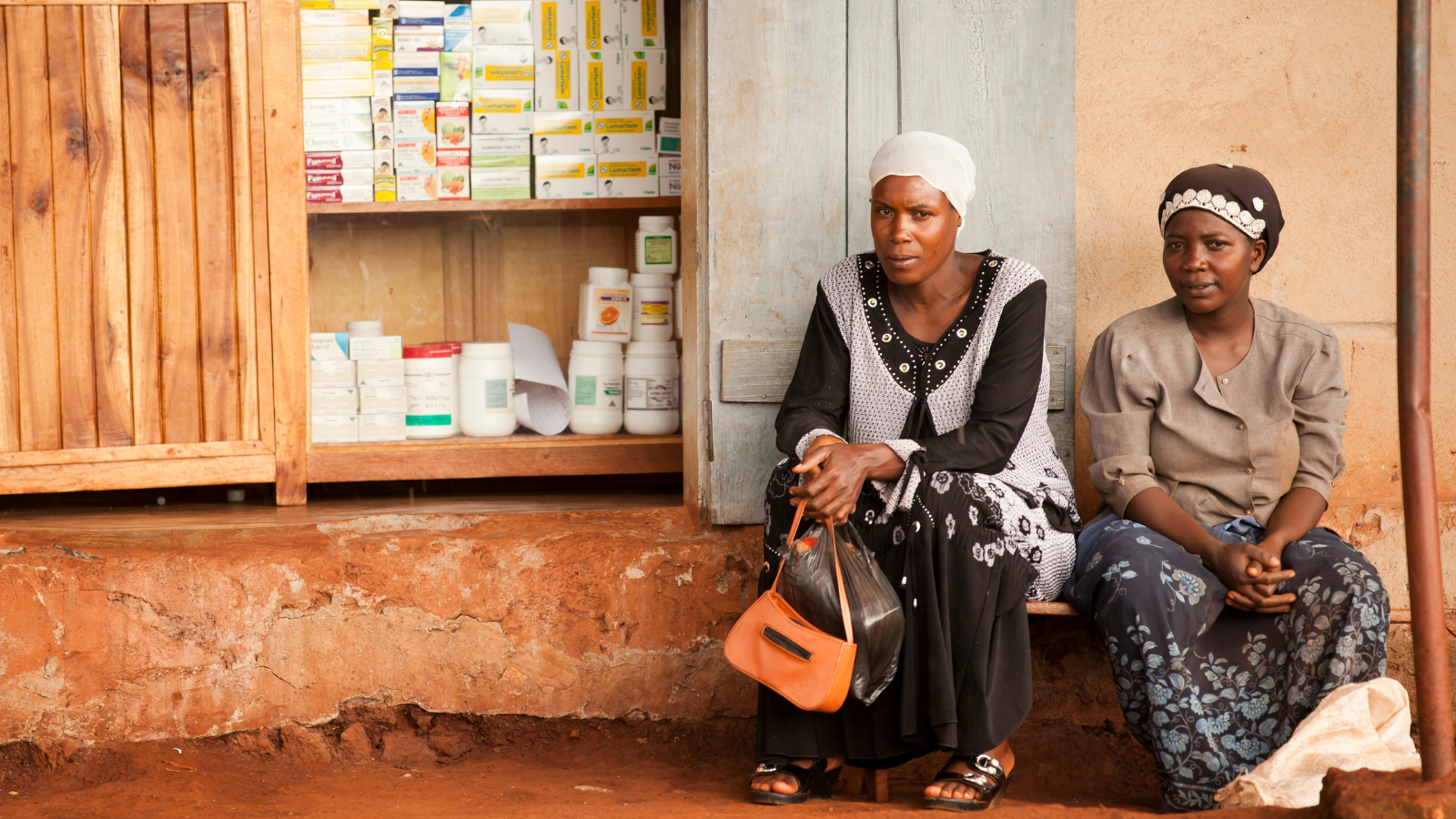 Two Ugandan women sitting in front of a drug store